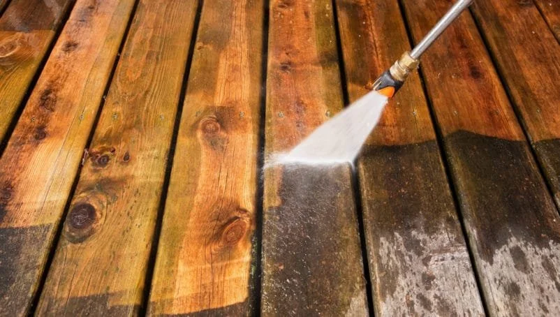 A pressure washer spraying water on stained wooden deck boards.