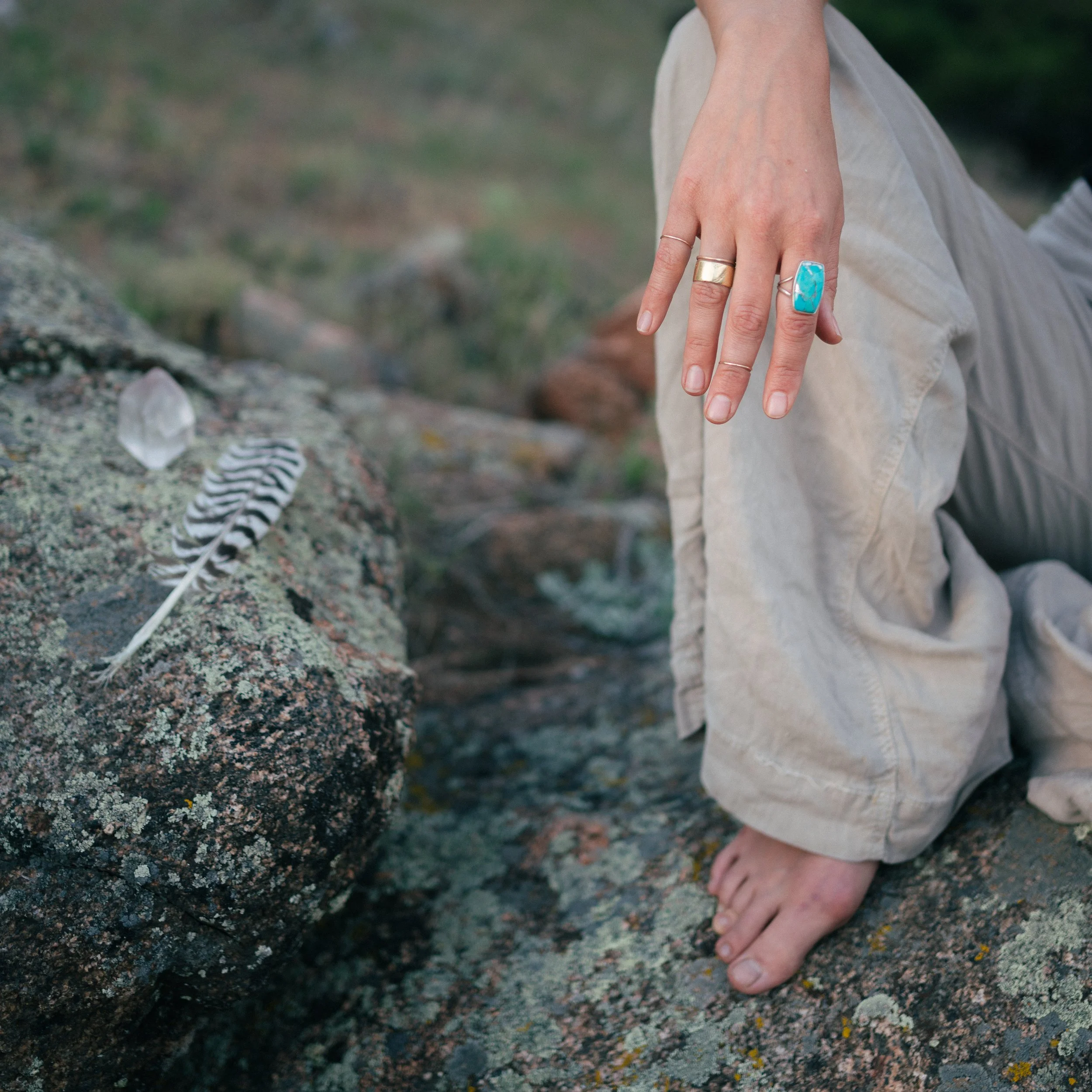 A person with rings on their fingers kneeling on rocky ground near a small fire with glow and smoke.