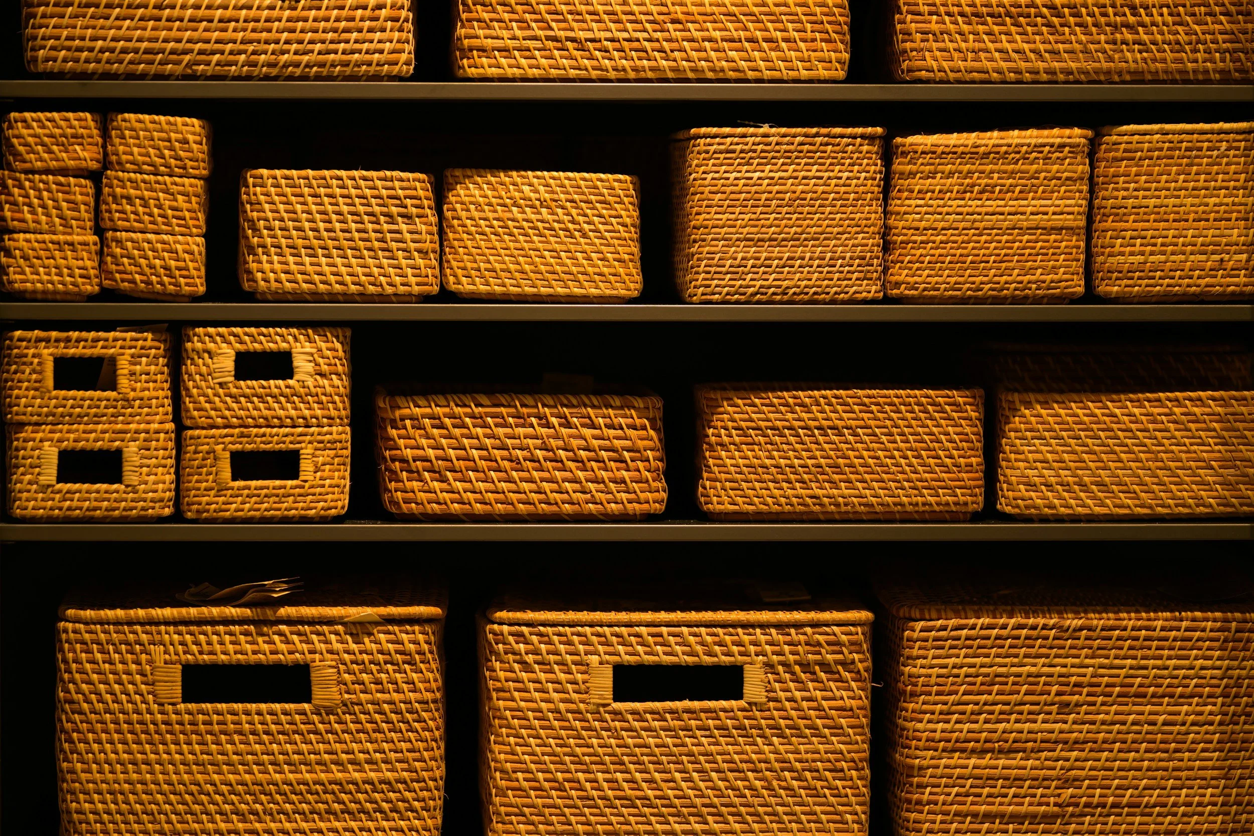 Display of multiple woven rattan baskets arranged on shelves, with various sizes and patterns.