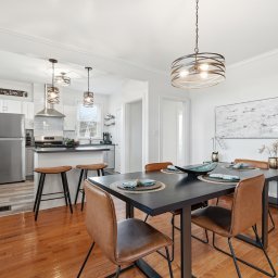 Modern kitchen and dining room with a black dining table, six brown chairs, pendant lights, and a view into the kitchen with white cabinets and a island.