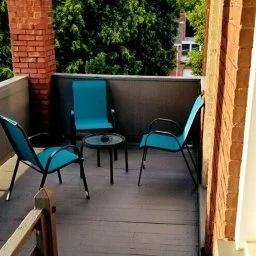 Outdoor balcony with four chairs and a small table, surrounded by brick walls and greenery in the background.