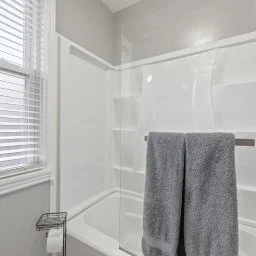 White bathtub with a gray towel hanging on a bar, bathroom with white window blinds and gray walls.