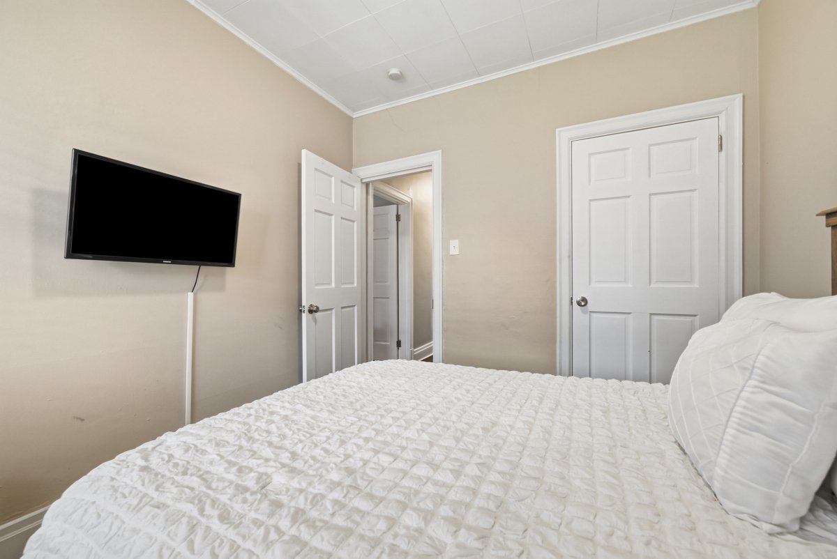 A bedroom with a bed, a wall-mounted TV, and two closed white doors.