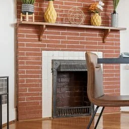 Brick fireplace with a wooden mantel decorated with vases and plants, in a living room setting.