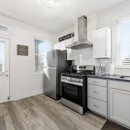Modern kitchen with gray cabinets, stainless steel refrigerator, black stove, and white walls with windows.
