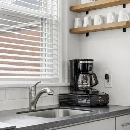 Kitchen window with blinds, coffee maker on countertop, shelves with white mugs