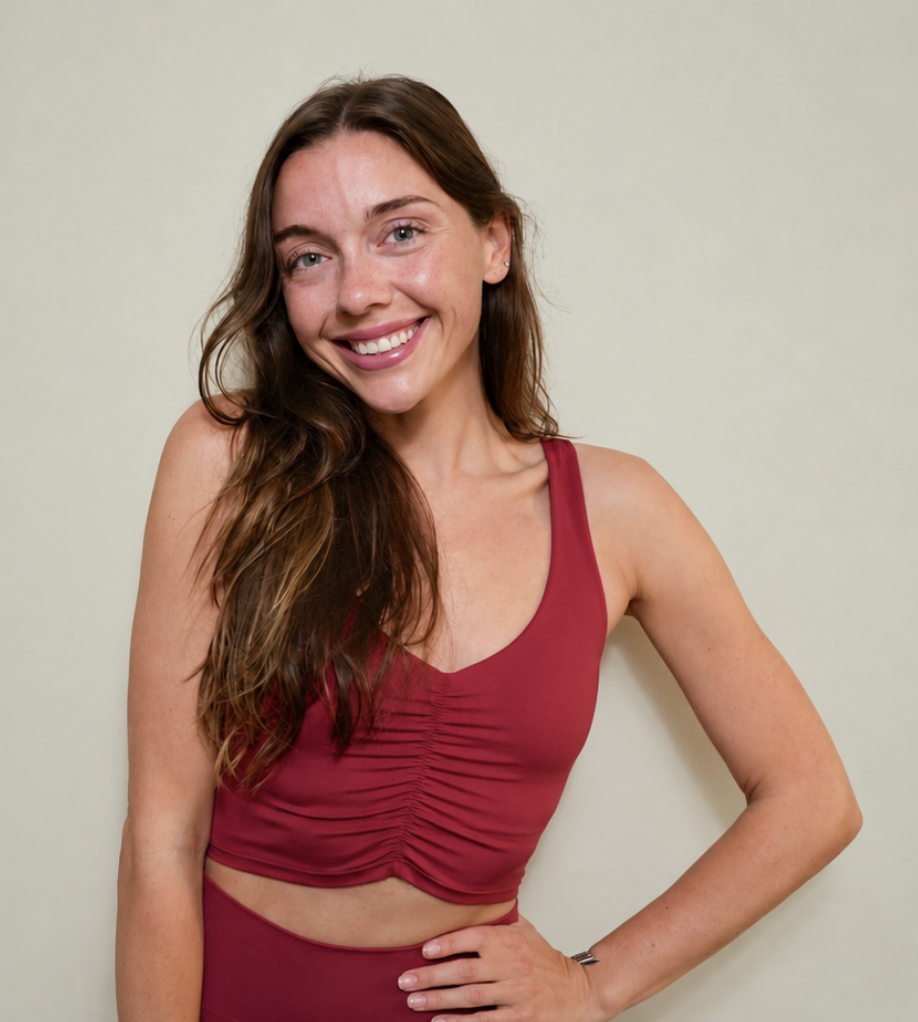 A woman with long, light brown hair, wearing a black bikini top and black shorts, standing in front of a white door, smiling with her hands on her hips.