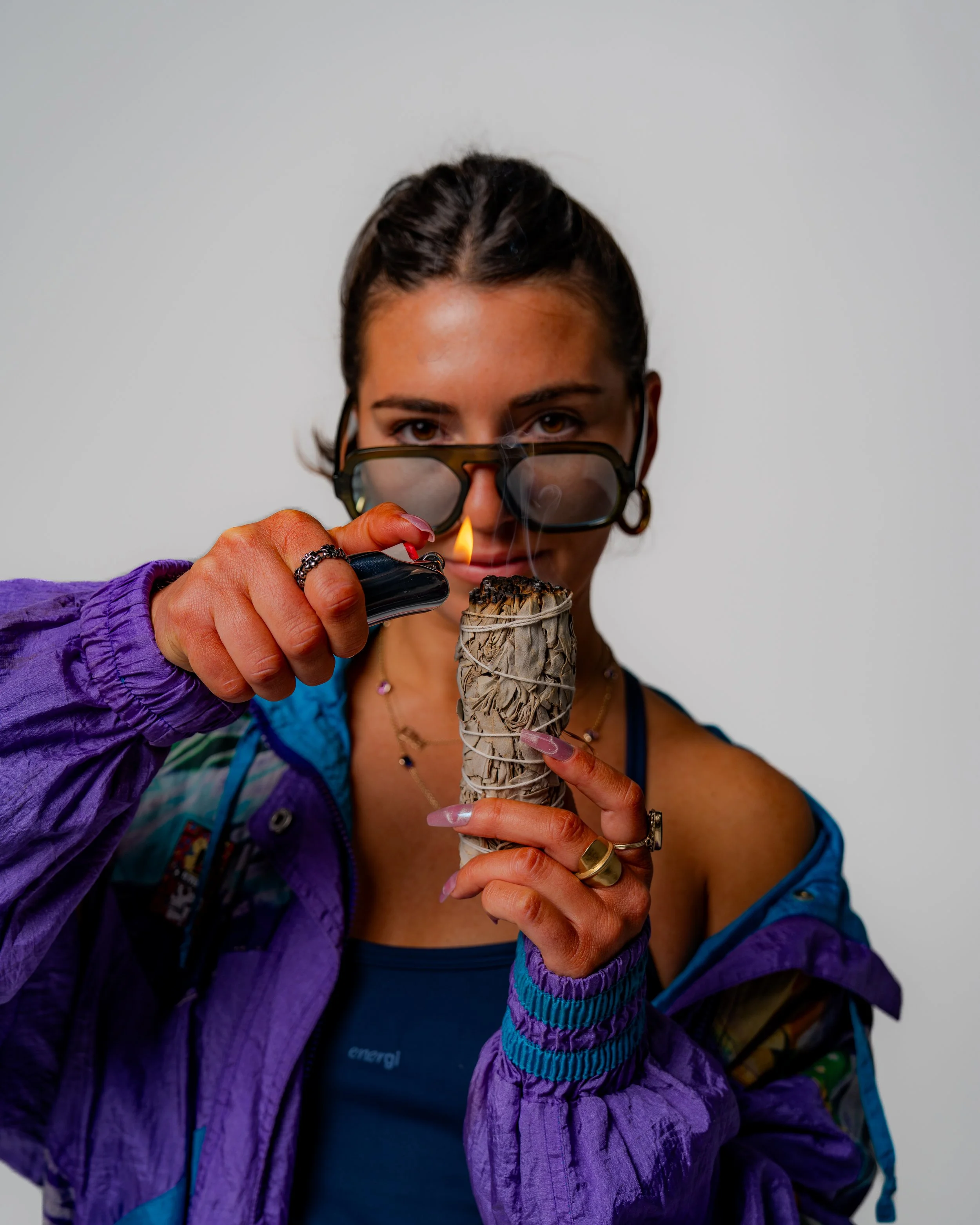 A person with dark hair and glasses holding a lit firework with a neutral background.