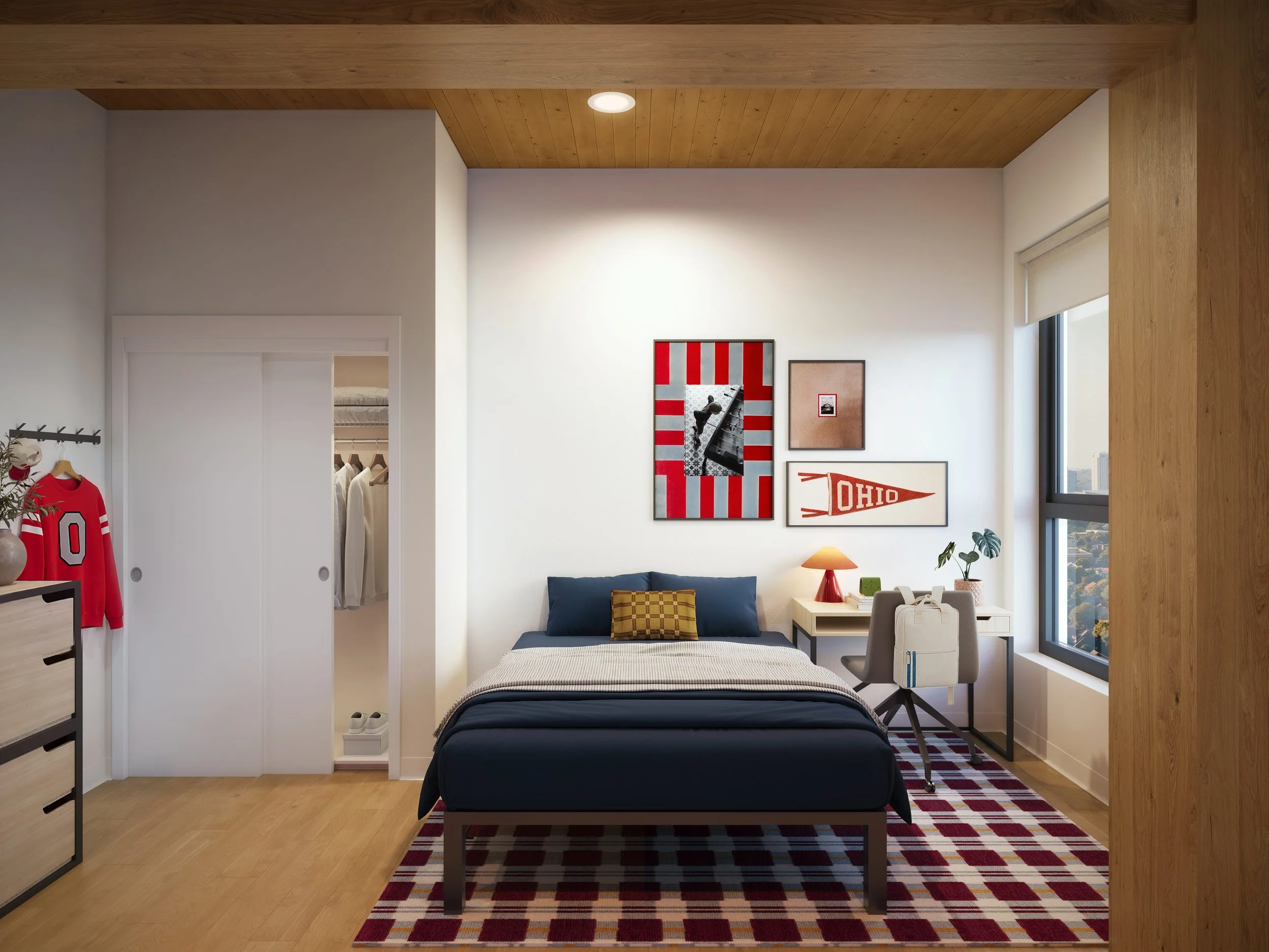 A bedroom with a bed, wall art, a window, and a small side table with a lamp. The room has light-colored walls, a wooden ceiling, and a patterned rug on the floor.