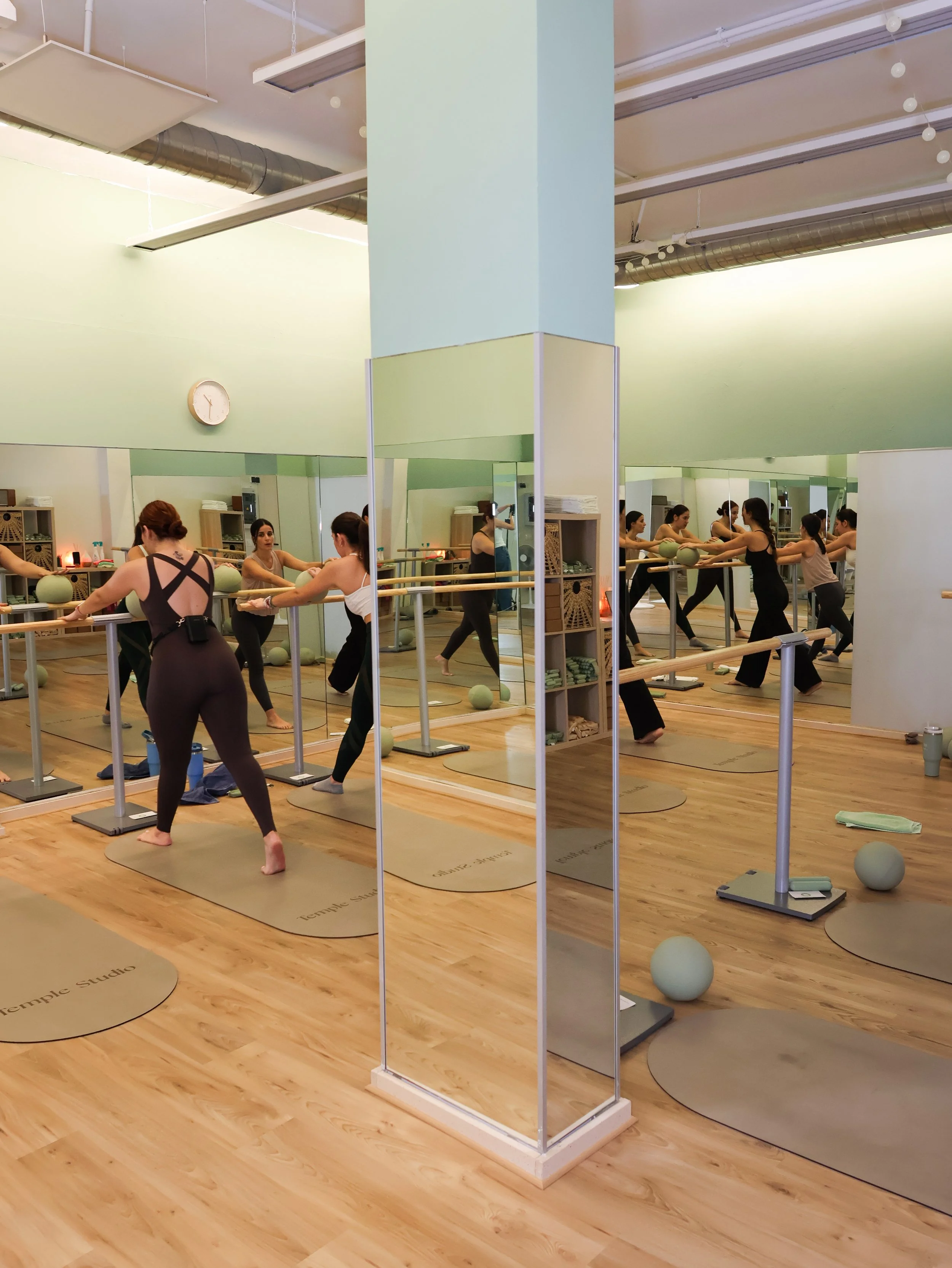 Varias personas haciendo ejercicio de ballet en un estudio con espejos y suelo de madera, en un entorno luminoso y moderno.