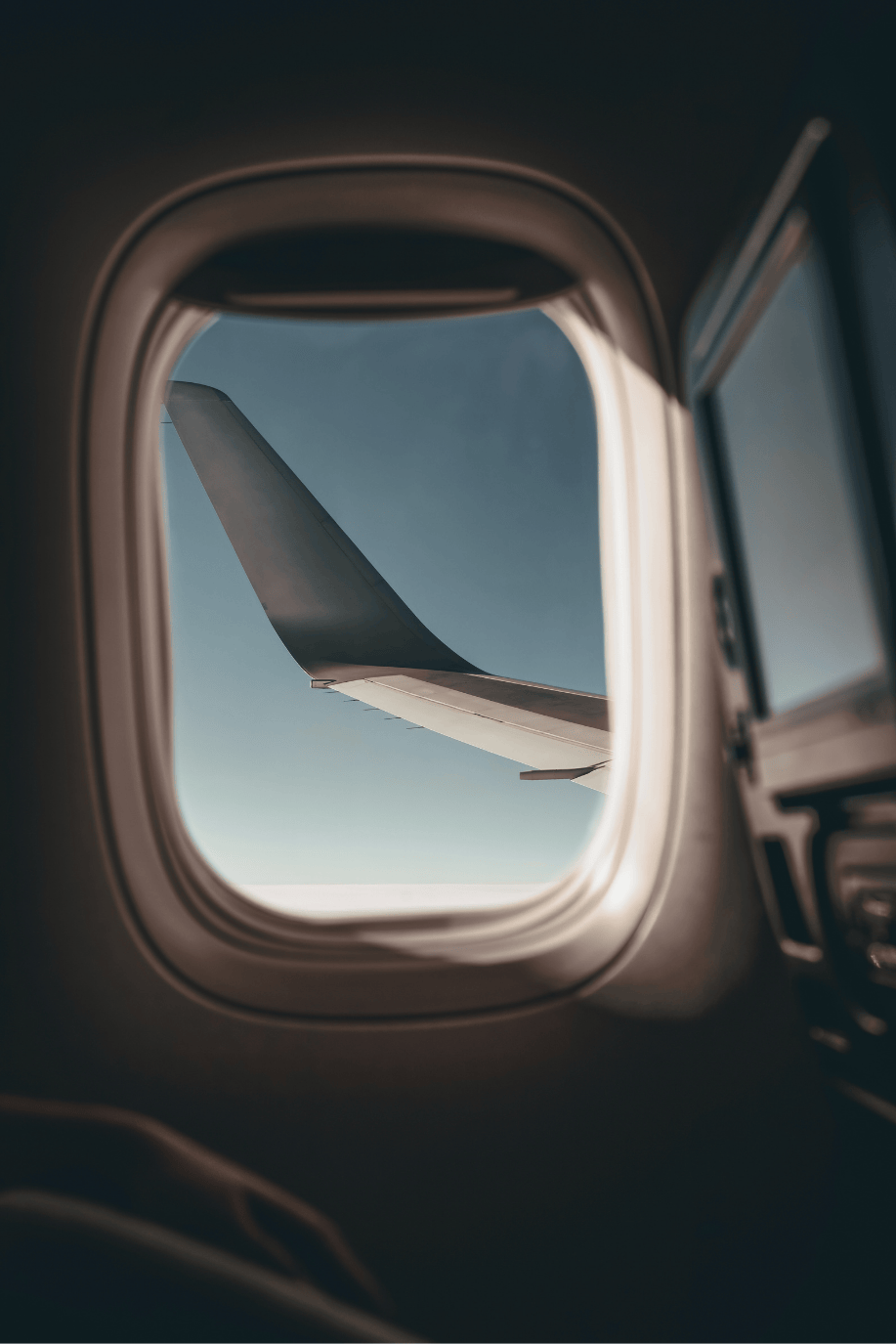View of an airplane wing seen through an airplane window in flight.