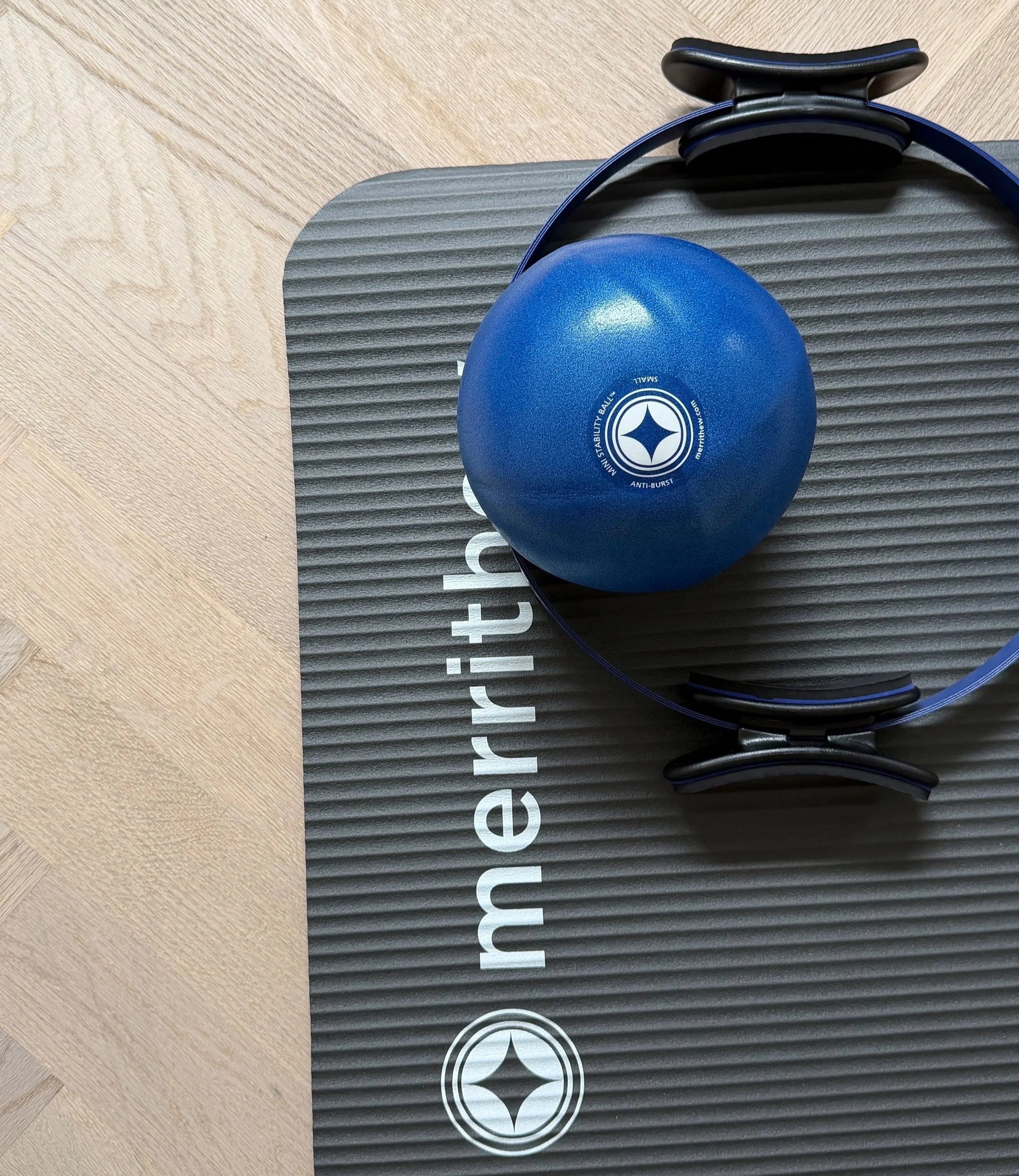 Blaue Pilates Ball und Pilates Circle auf schwarzer Merrithew Pilates Matte, auf Holzfussboden