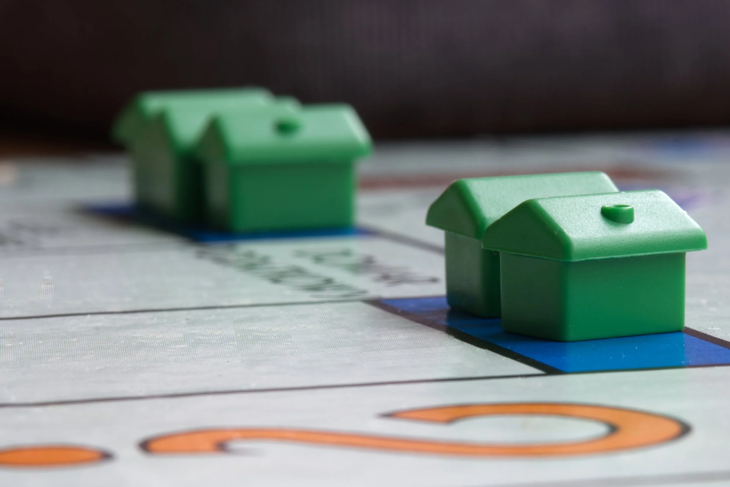 Close-up of green plastic houses as game pieces on a Monopoly game board.