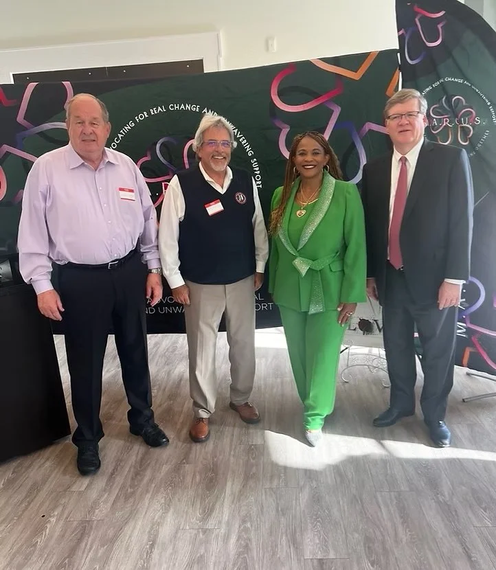 Four people standing together in front of a black and colorful LGBTQ+ themed banner, smiling for a photo at an event.