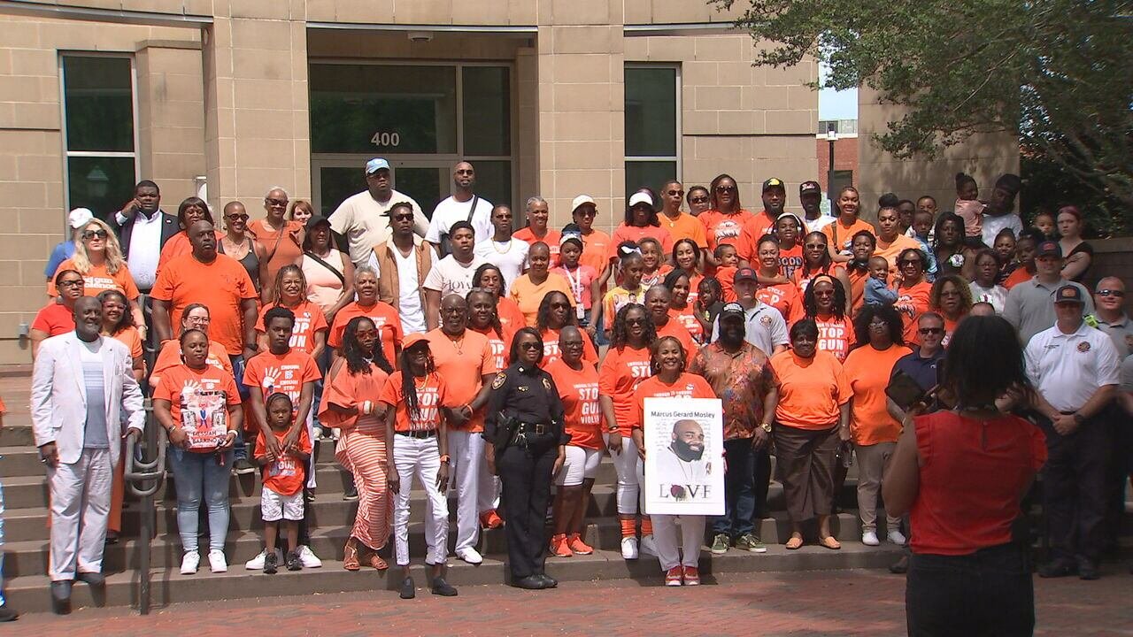 Group of people gathered on steps in front of a building, participating in a demonstration or rally, many wearing orange shirts with some holding signs advocating against gun violence.