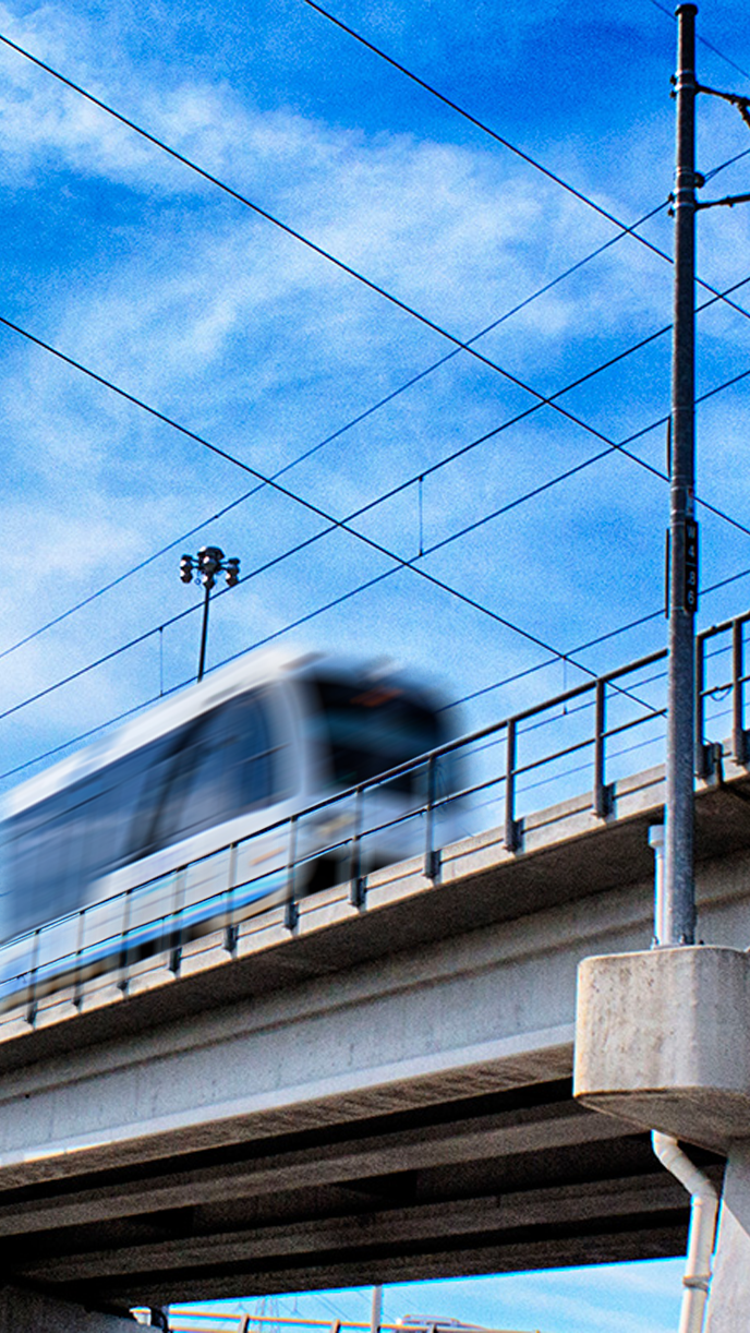 A moving train on an elevated railway track with blue sky and clouds in the background.