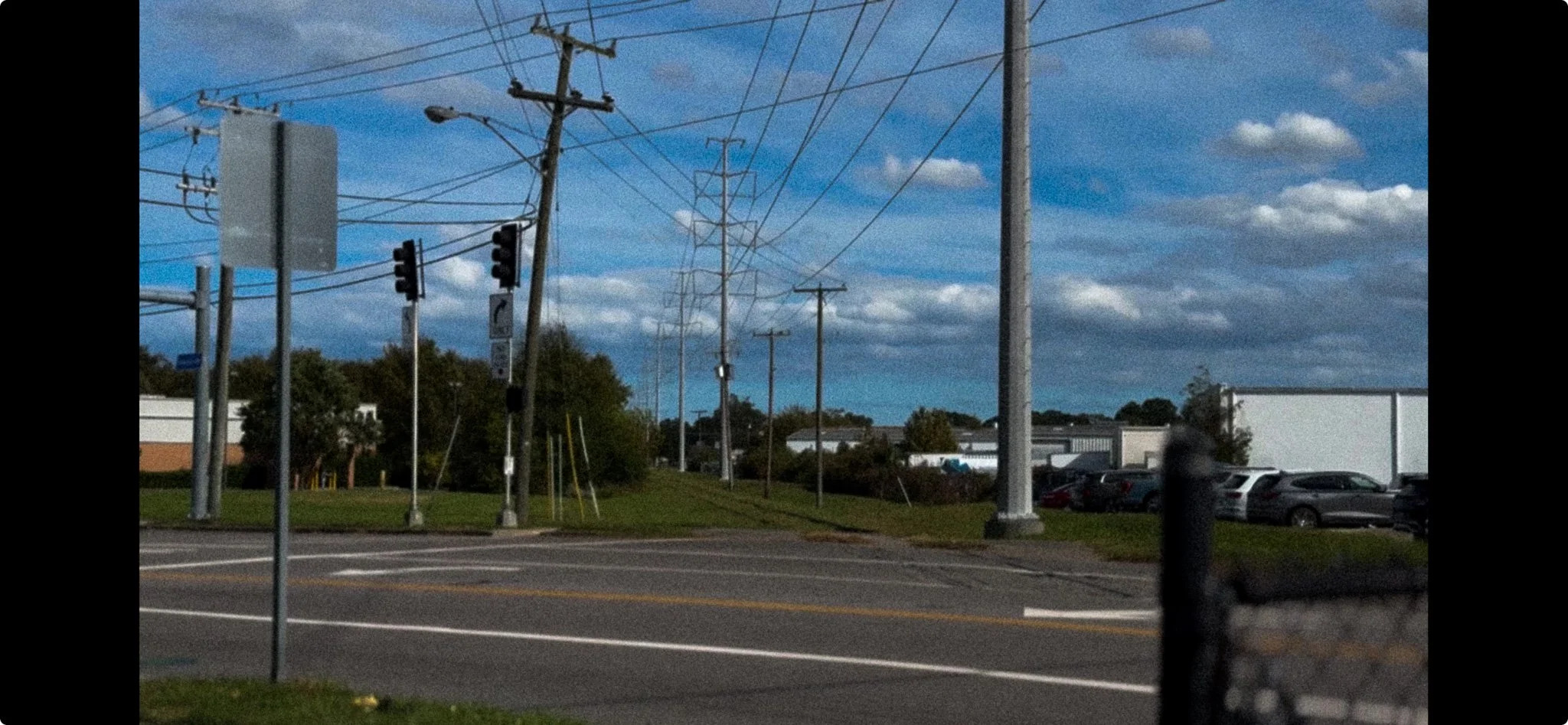 Street scene with utility poles, power lines, traffic lights, parked cars, on a partly cloudy day. At border of Virginia beach at Newtown Road.