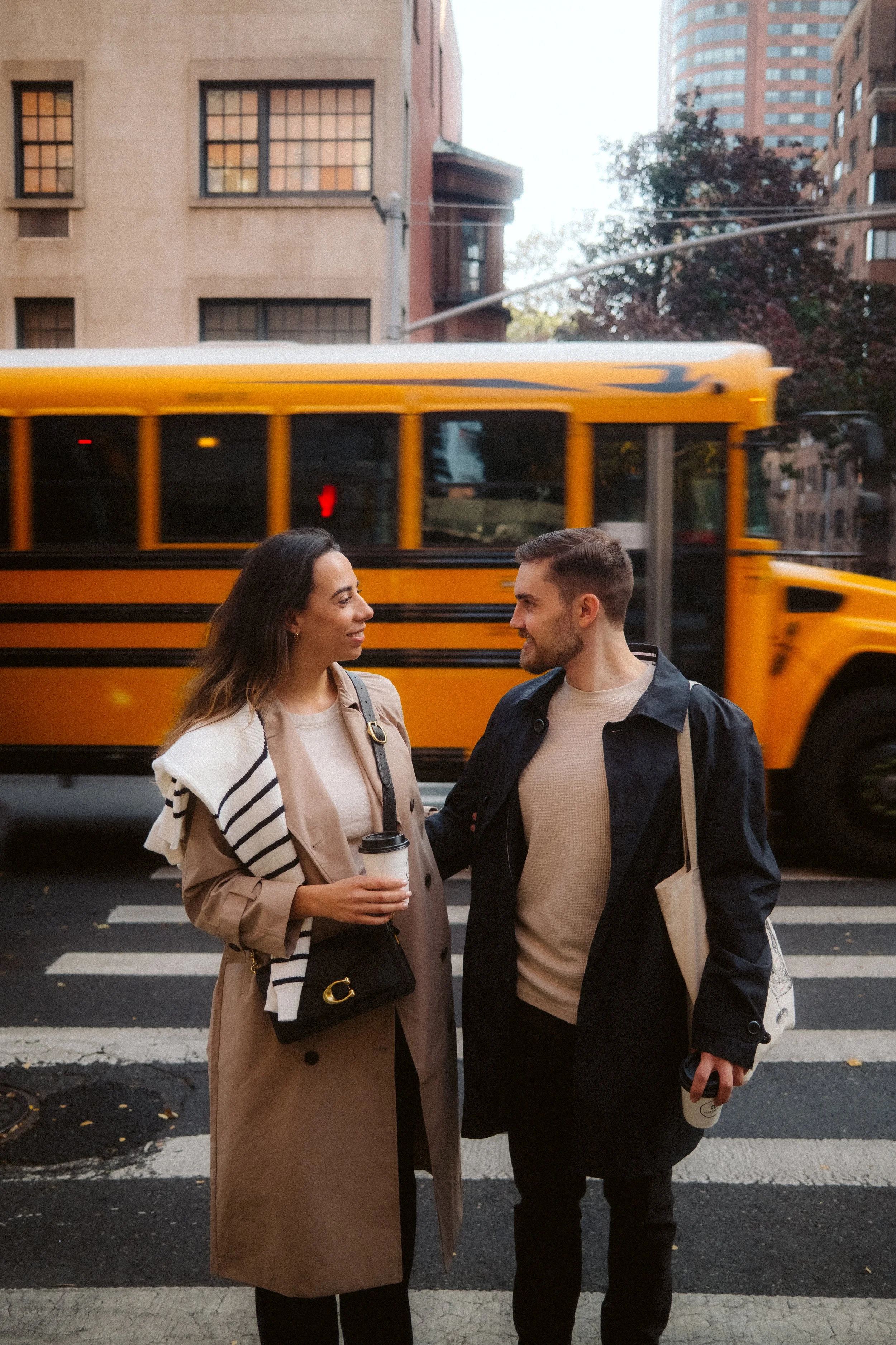 Young people talking on the street in front of a building, with a yellow bus in the background.