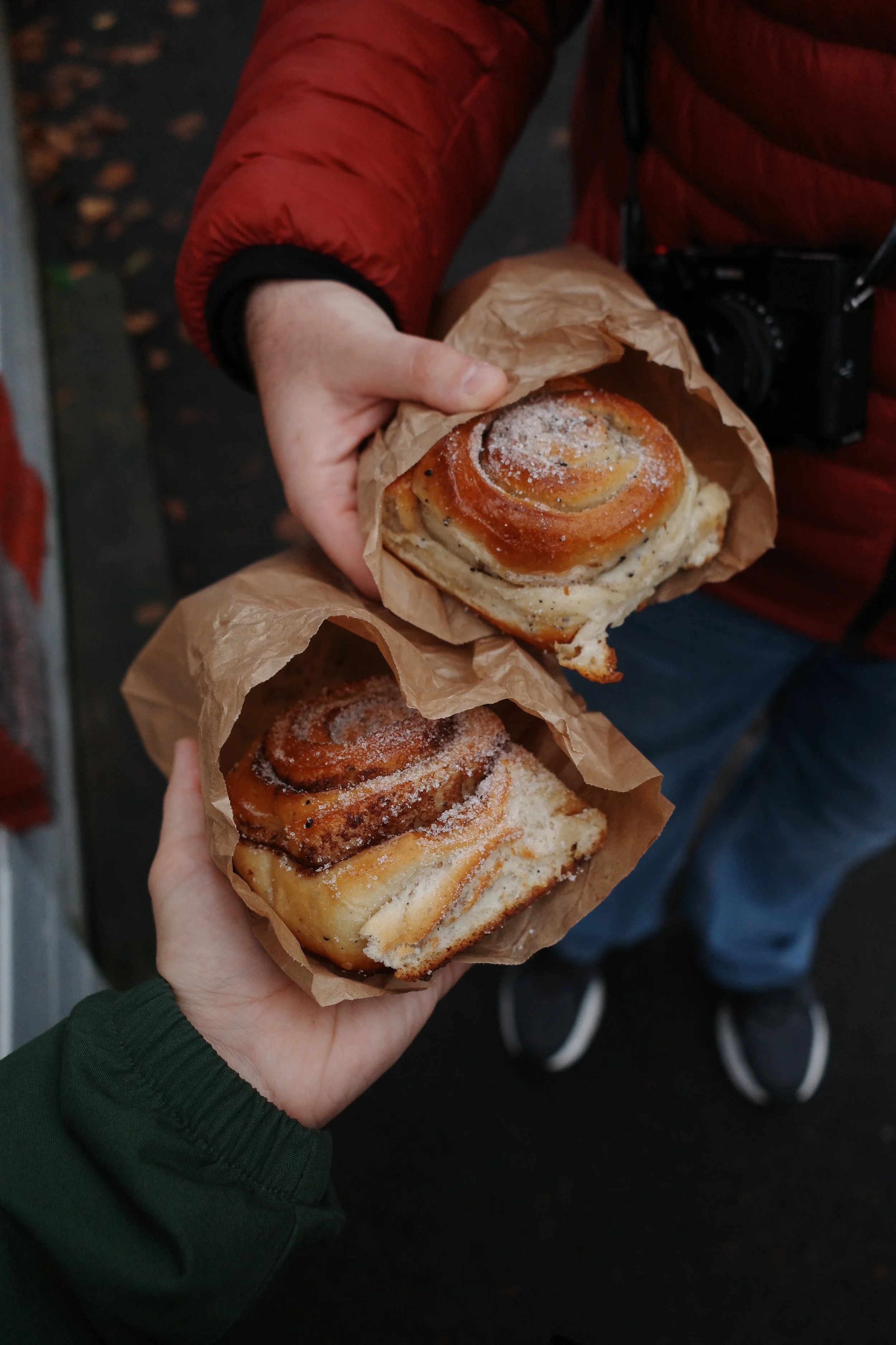 Person holding two cinnamon rolls wrapped in kraft paper, one topped with sugar.