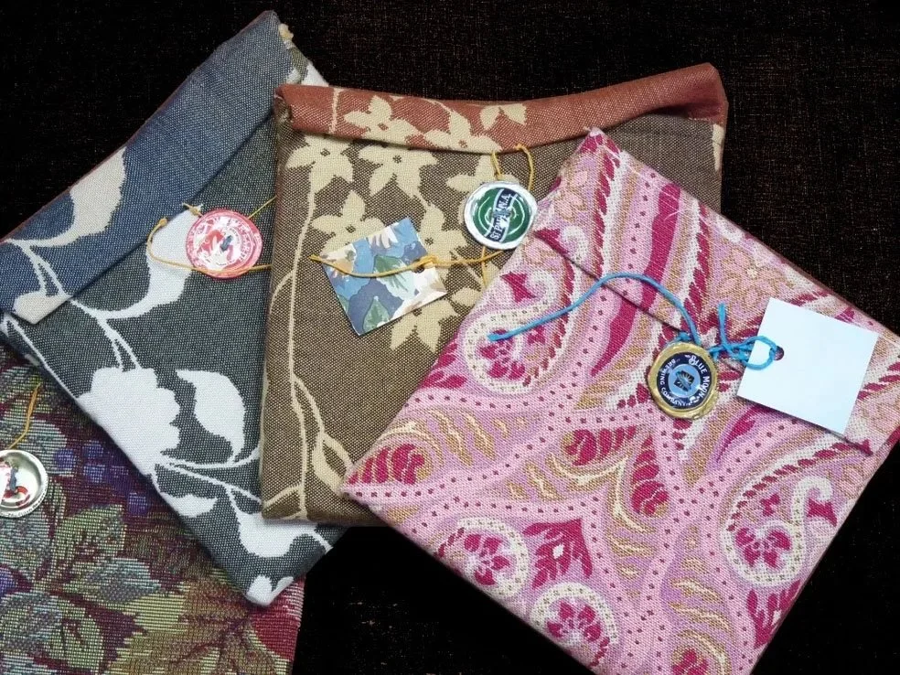 Three folded fabrics with floral and paisley patterns, each with a parasol-shaped souvenir tag attached with a string, placed on a dark surface.