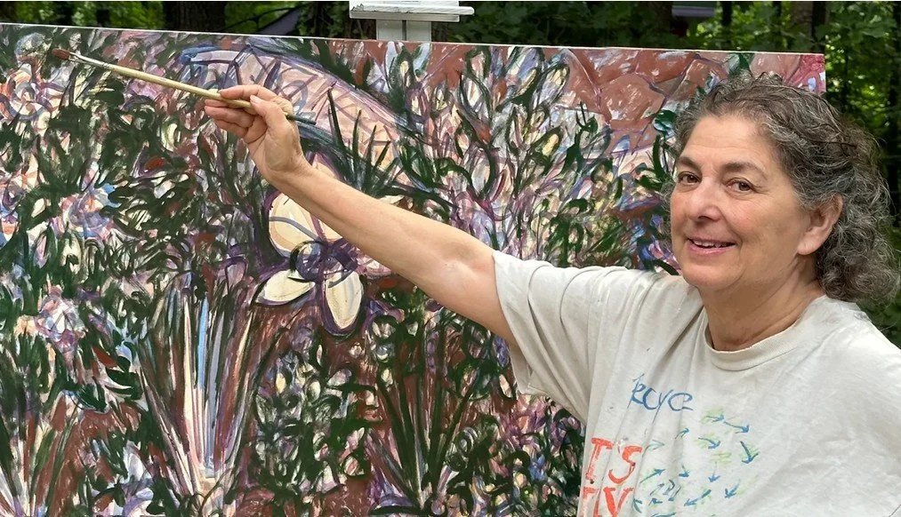 Woman painting an abstract floral artwork outdoors with a brush