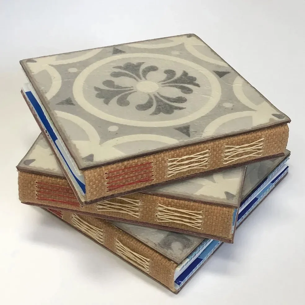 Three decorative hardcover books with patterned covers stacked on a white surface.
