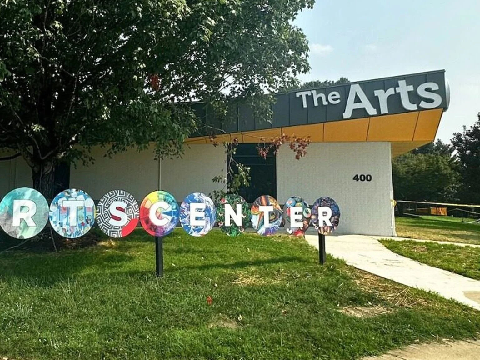 Sign for The Arts center with colorful letters on circular backgrounds spelling 'ARTS CENTER' in front of building with address 400.
