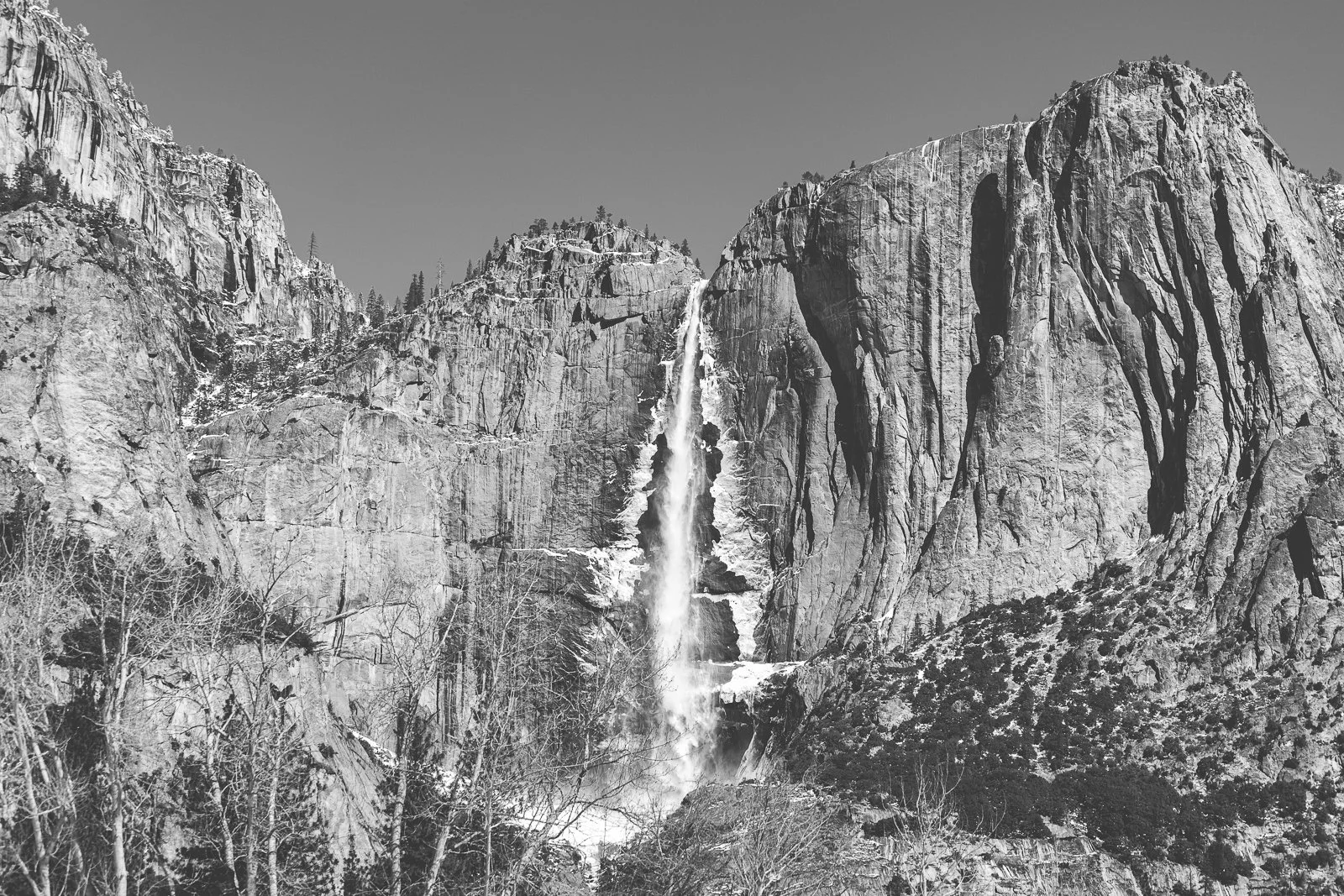Cascade au milieu d'une montagne rocheuse, arbres en premier plan, ciel clair.