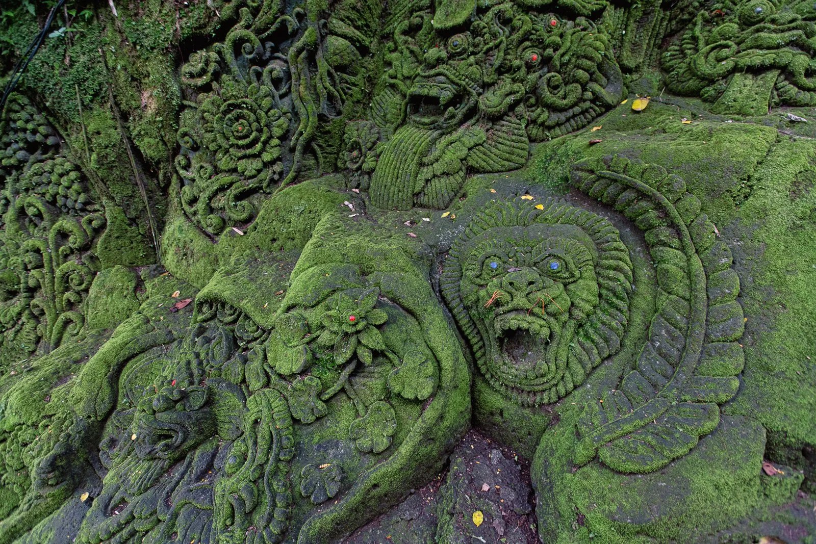 Détails de sculptures en pierre recouvertes de mousse représentant des têtes de lion et des créatures mythologiques dans un style fantasy.