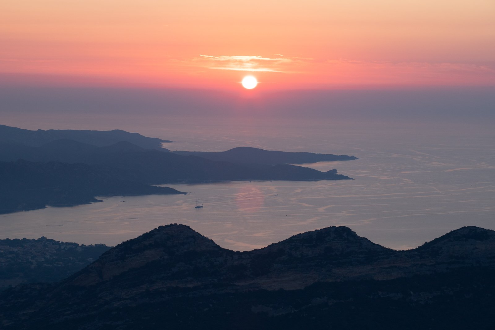 Coucher de soleil sur une mer calme avec des îles et des montagnes sombres en premier plan, ciel teinté de rose et orange.