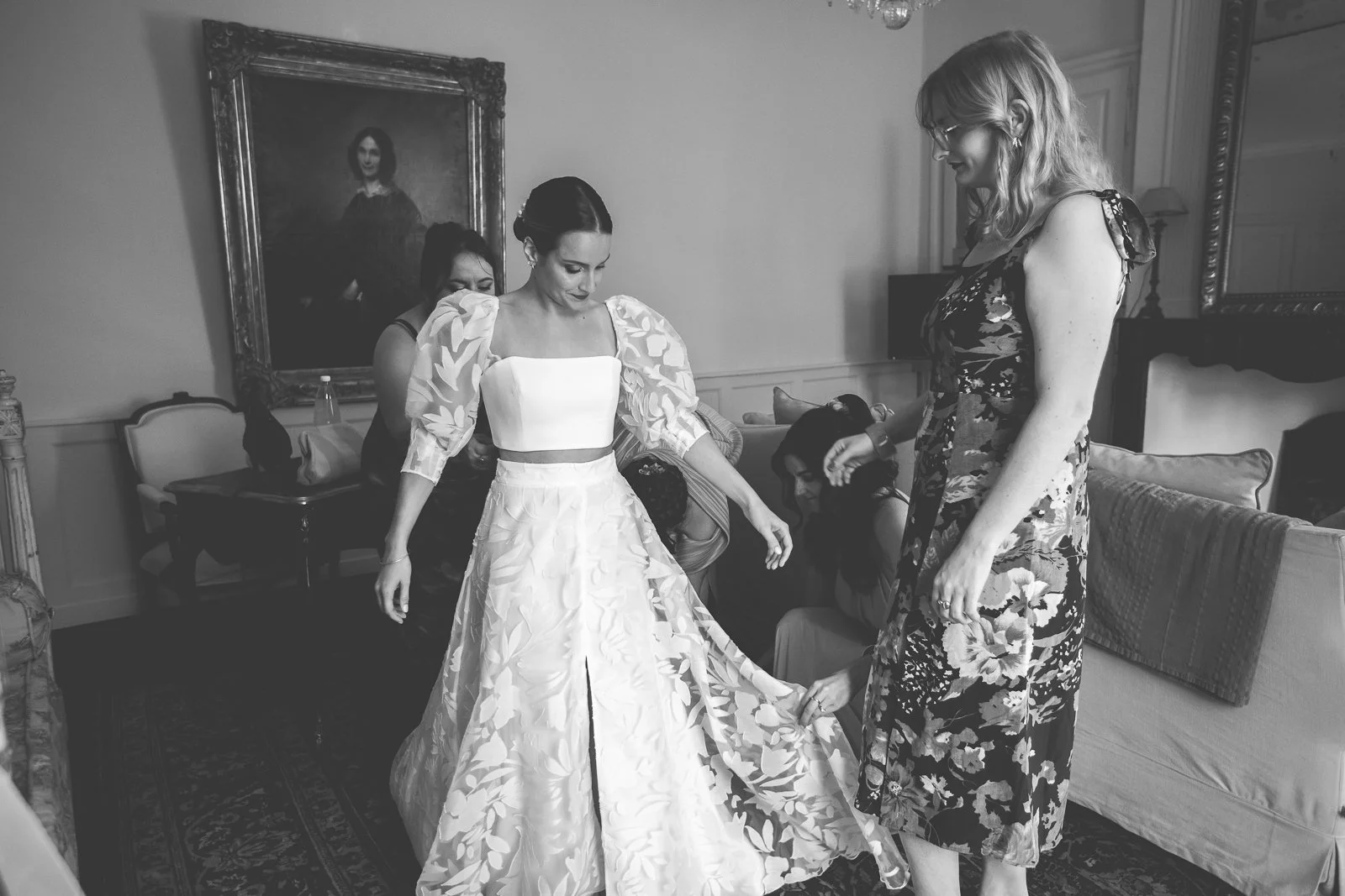 Femme en robe de mariée aidée par une autre femme dans une pièce élégante