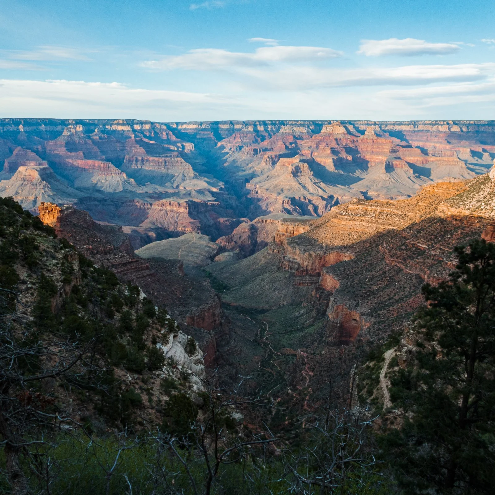 Vue du Grand Canyon avec des formations rocheuses colorées, sous un ciel bleu avec quelques nuages.