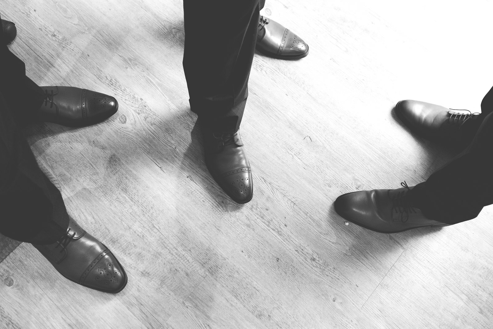 Cté d'hommes portant des chaussures en cuir formelles, se tenant en cercle, vu du dessus, sur un sol en bois.