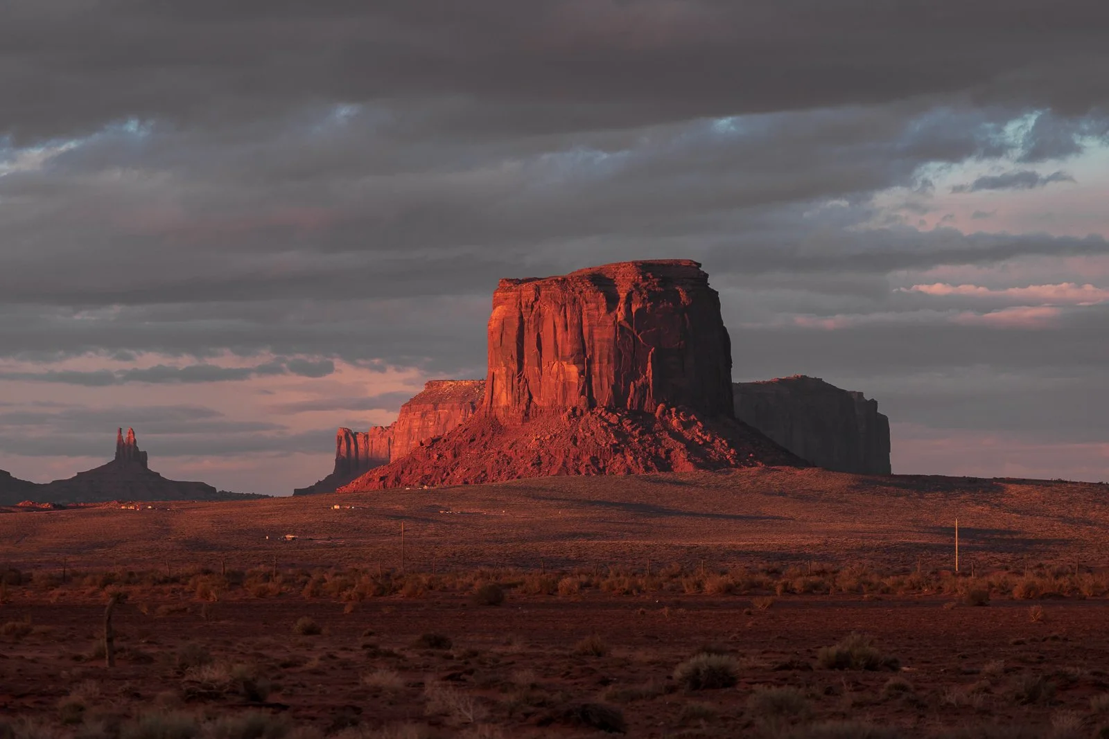 Monument Valley, formations rocheuses rouges sous un ciel nuageux au coucher du soleil.