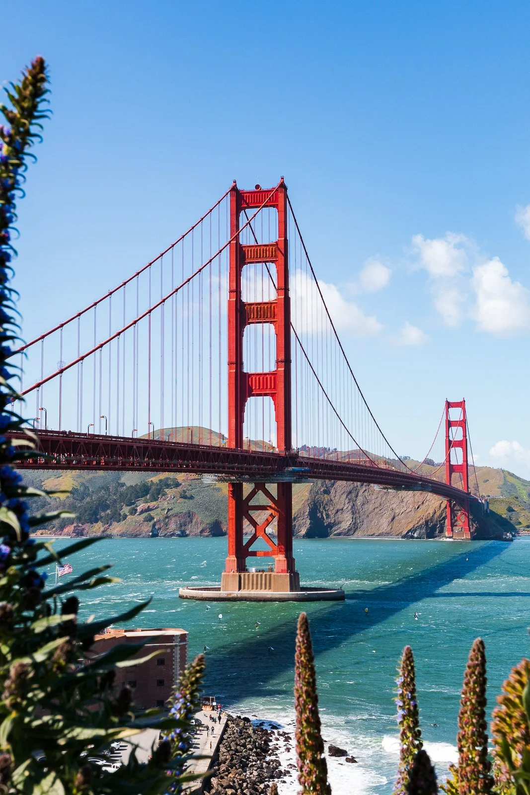 Le pont Golden Gate rouge sur l'océan avec des collines en arrière-plan, ciel bleu et quelques nuages.