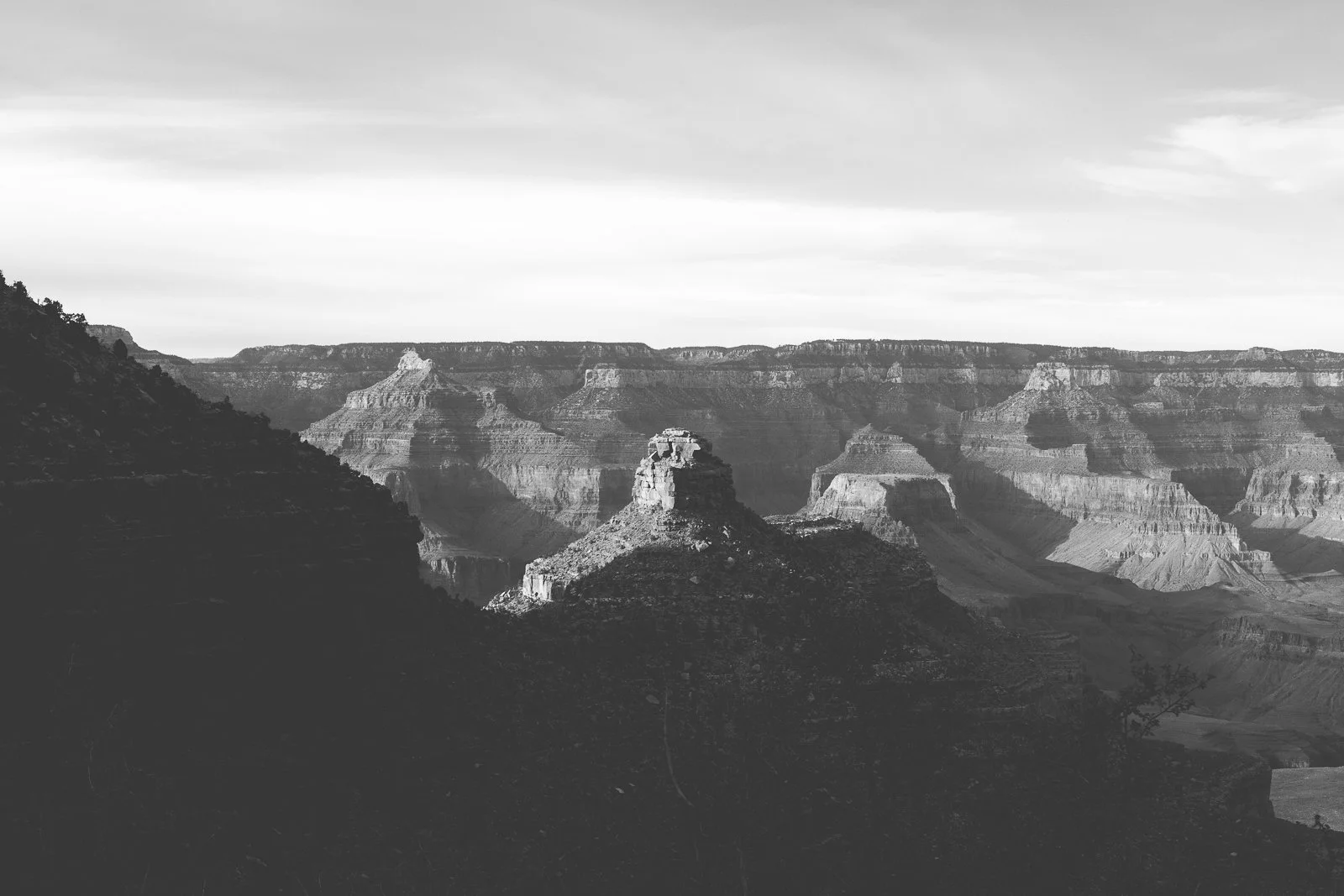 Photo en noir et blanc du Grand Canyon avec des formations rocheuses en relief et un ciel nuageux.