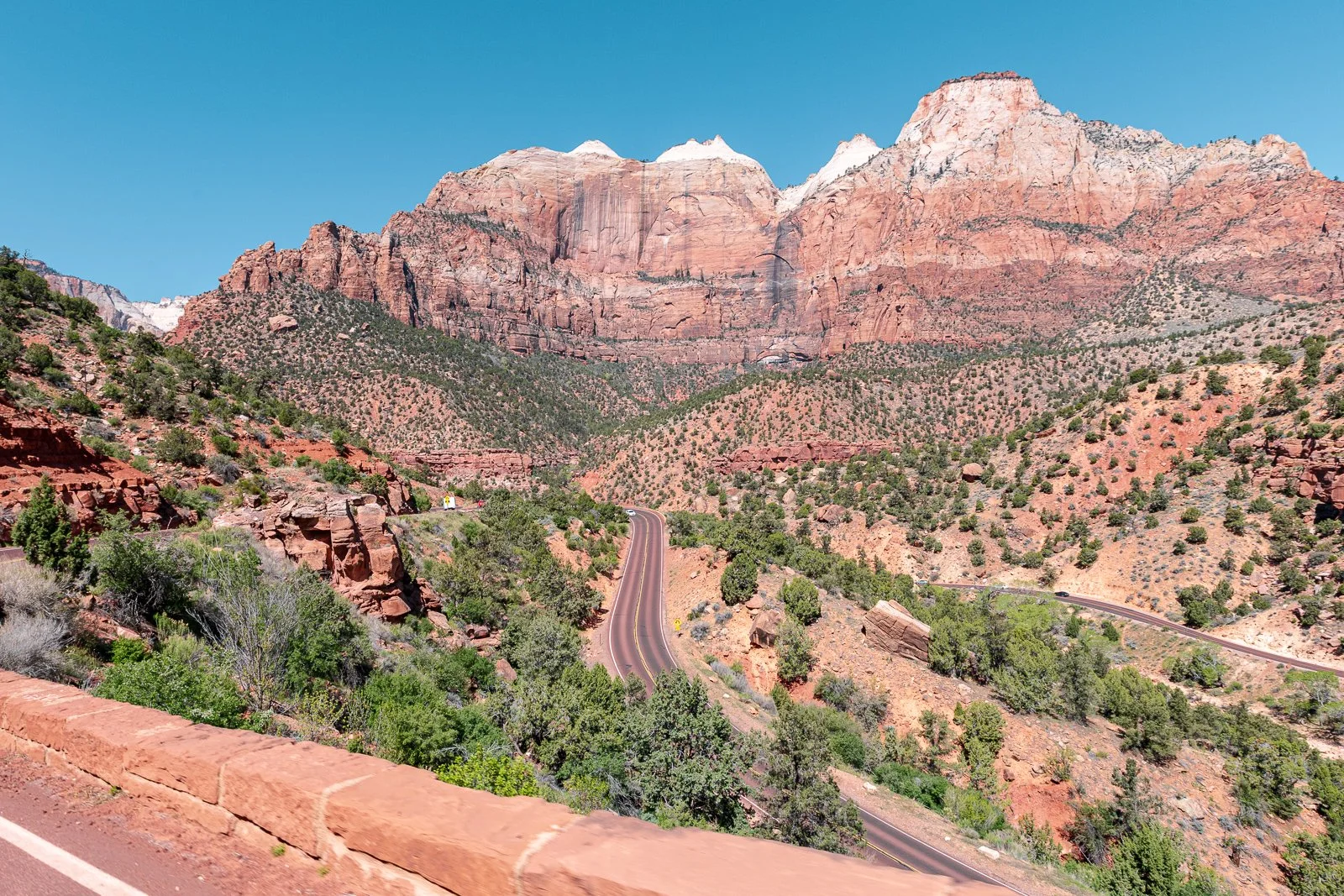 Montagnes rouges avec un ciel bleu, route sinueuse dans le canyon et végétation sparse.