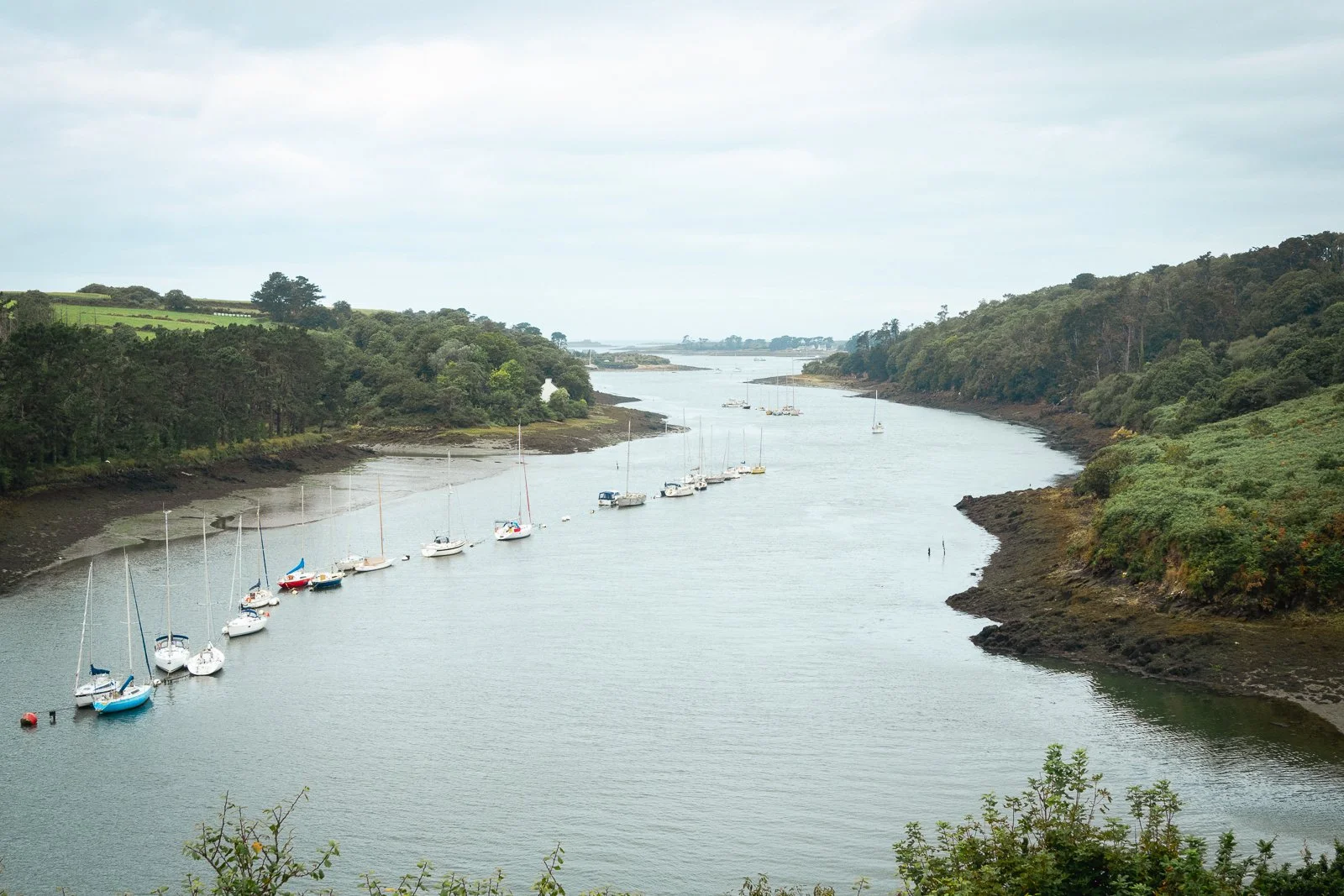 Vue d'une rivière bordée de collines verdoyantes avec plusieurs bateaux amarrés le long de la rive.