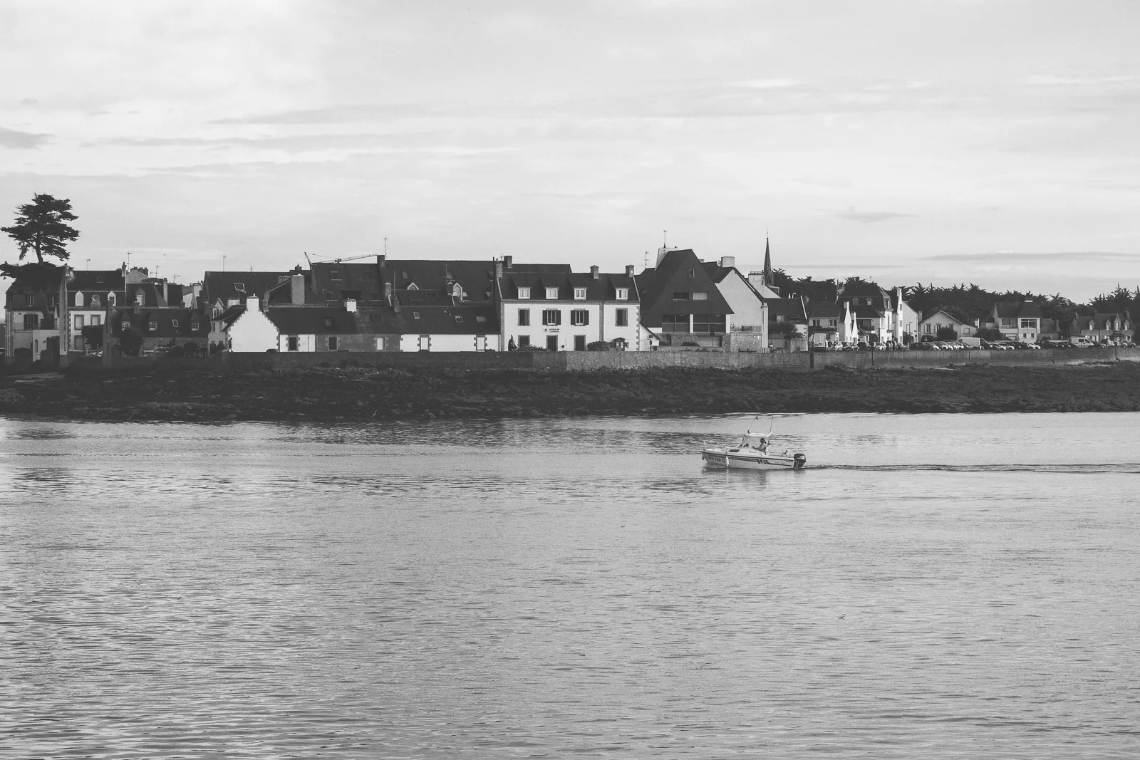 Vue d'une petite ville ou village au bord de l'eau avec des maisons et un bateau qui passe sur la rivière.