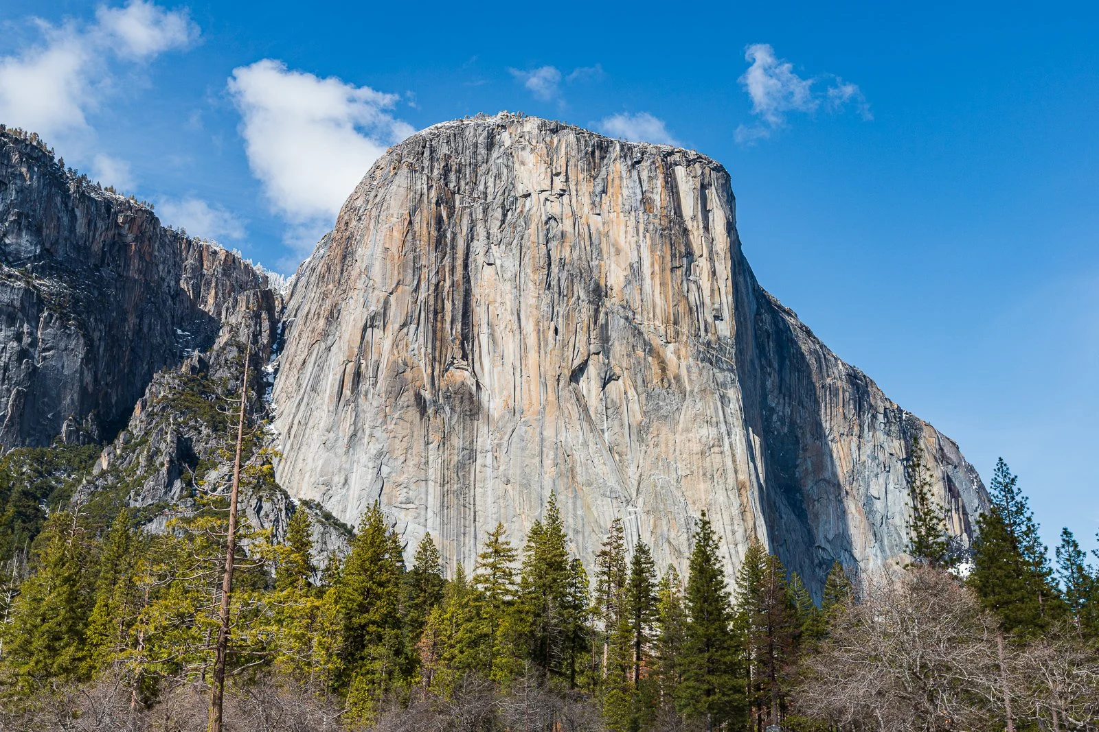 Une grande formation rocheuse en granite dans le parc national de Yosemite, entourée d'arbres verts et un ciel bleu avec quelques nuages.