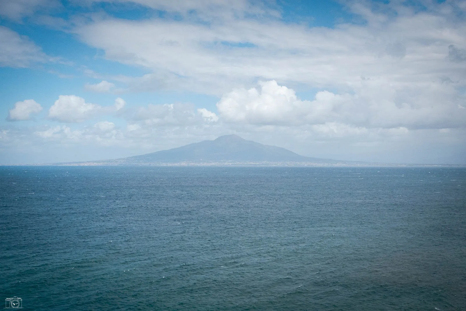 Vue d'une mer avec une île ou une montagne à l'horizon, ciel partiellement nuageux.
