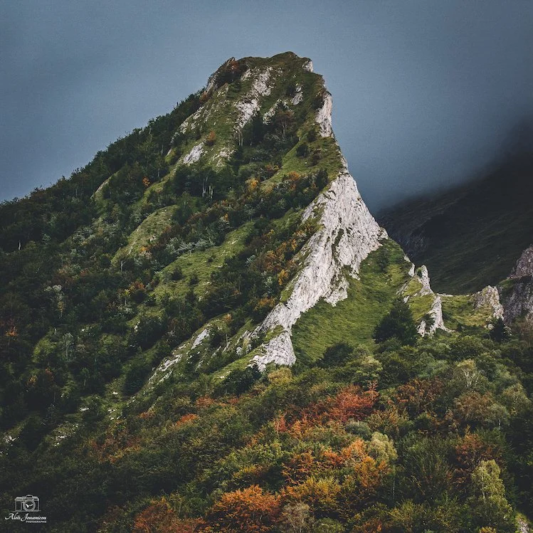 Montagne avec une pente rocheuse et une végétation dense, ciel sombre en arrière-plan.