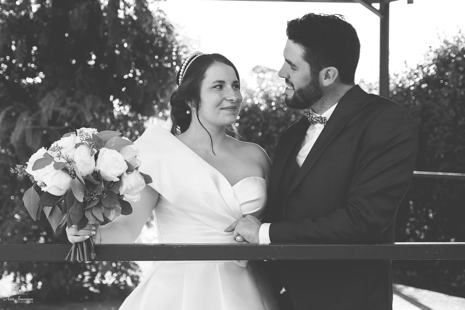 Un couple de mariés regarde tendrement l'un l'autre lors de leur mariage, en noir et blanc, avec un bouquet de fleurs dans la main de la mariée.