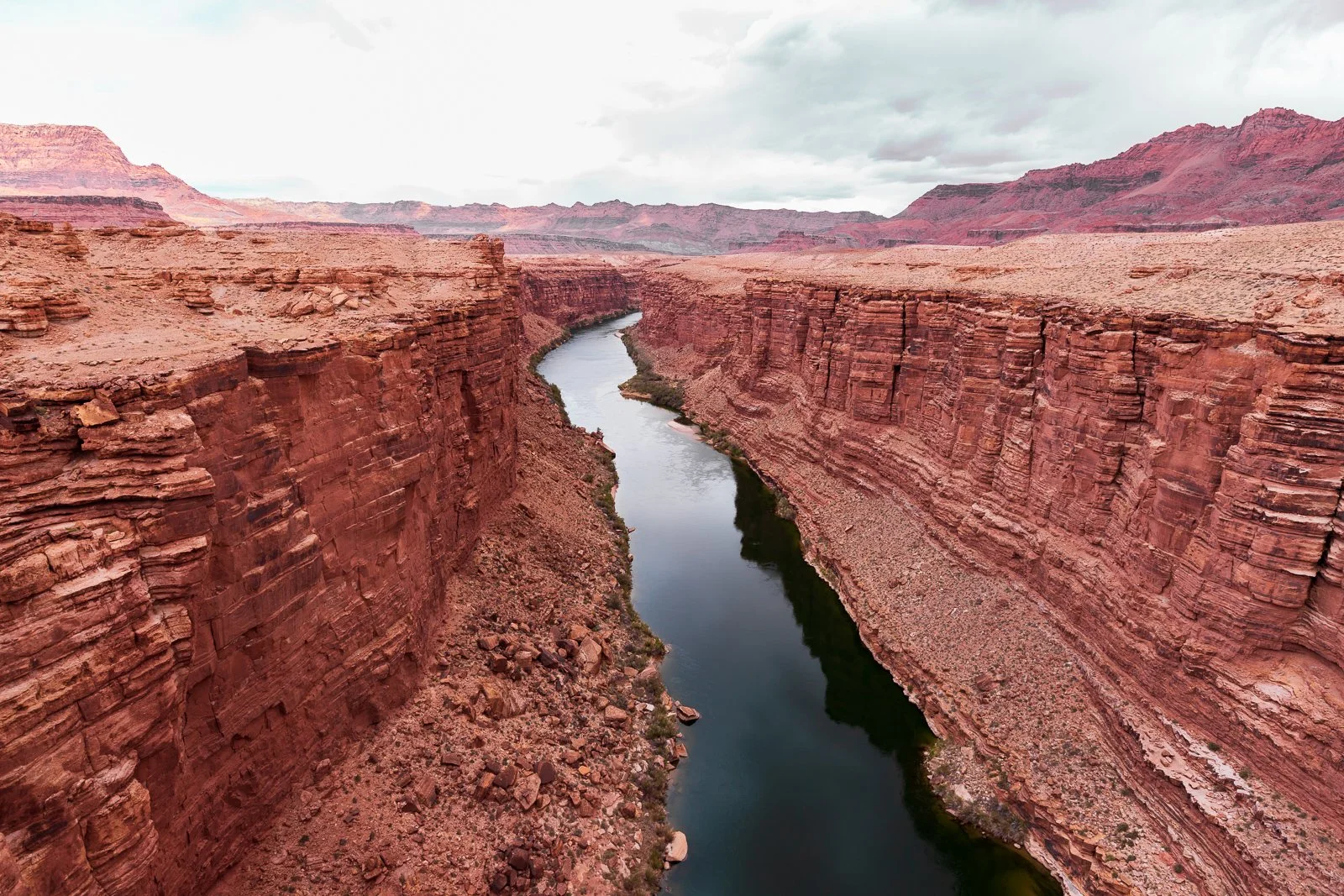Canyon avec un fleuve au fond, paysages rocheux et montagnes en arrière-plan, ciel nuageux