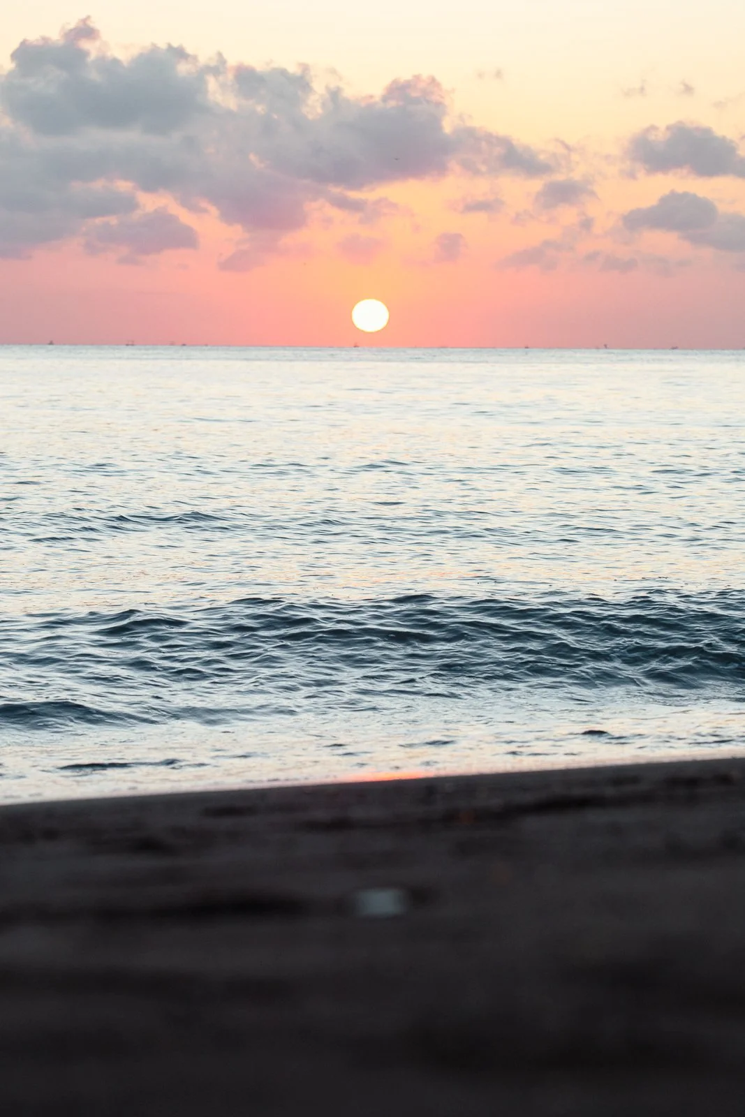 Coucher de soleil sur la mer avec des nuages roses et un ciel pastel.