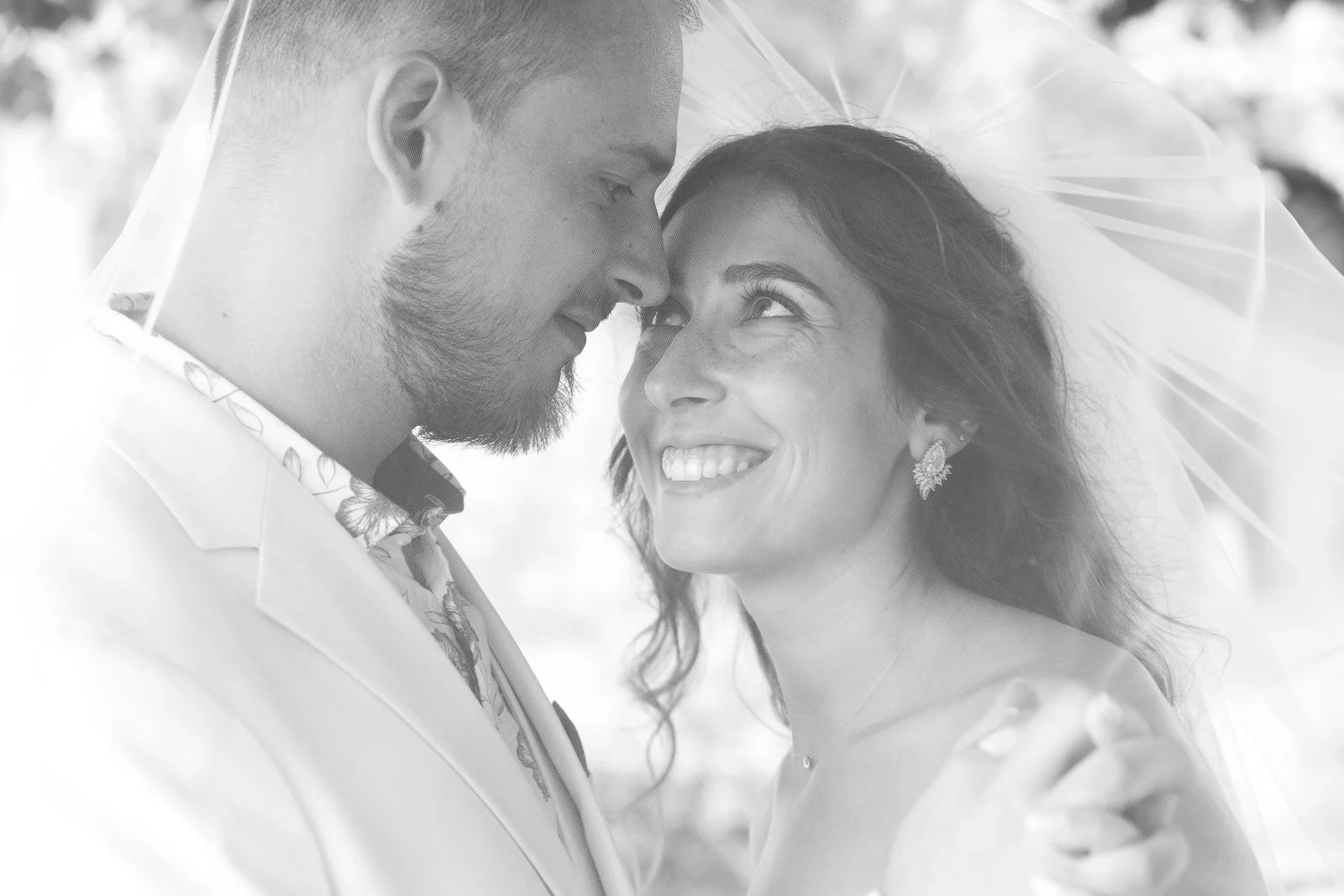 Un couple de mariés souriant lors de leur cérémonie avec un voile blanc transparent autour d'eux.