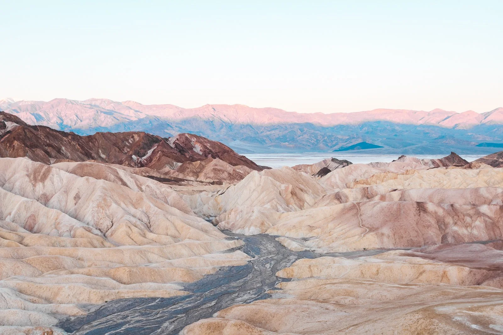 Paysage désertique avec des montagnes colorées et un sol rocheux, probablement de la vallée de la mort ou un lieu similaire.