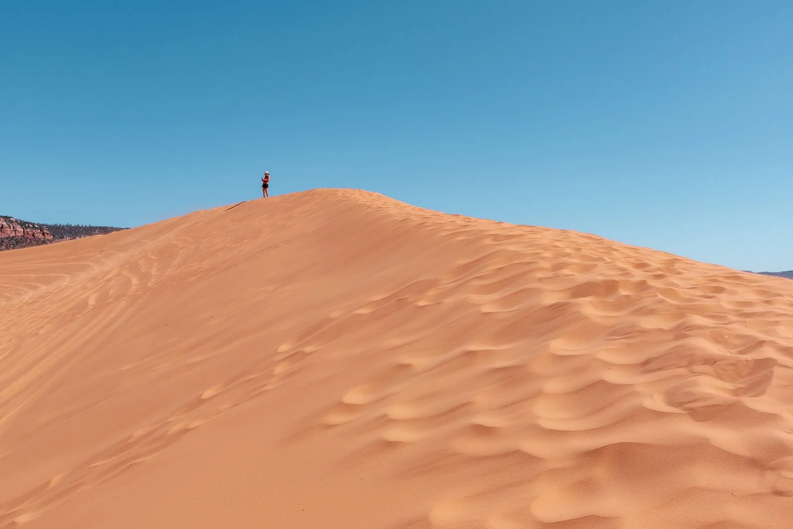 Une personne debout sur une dune de sable dans un désert avec un ciel bleu clair.