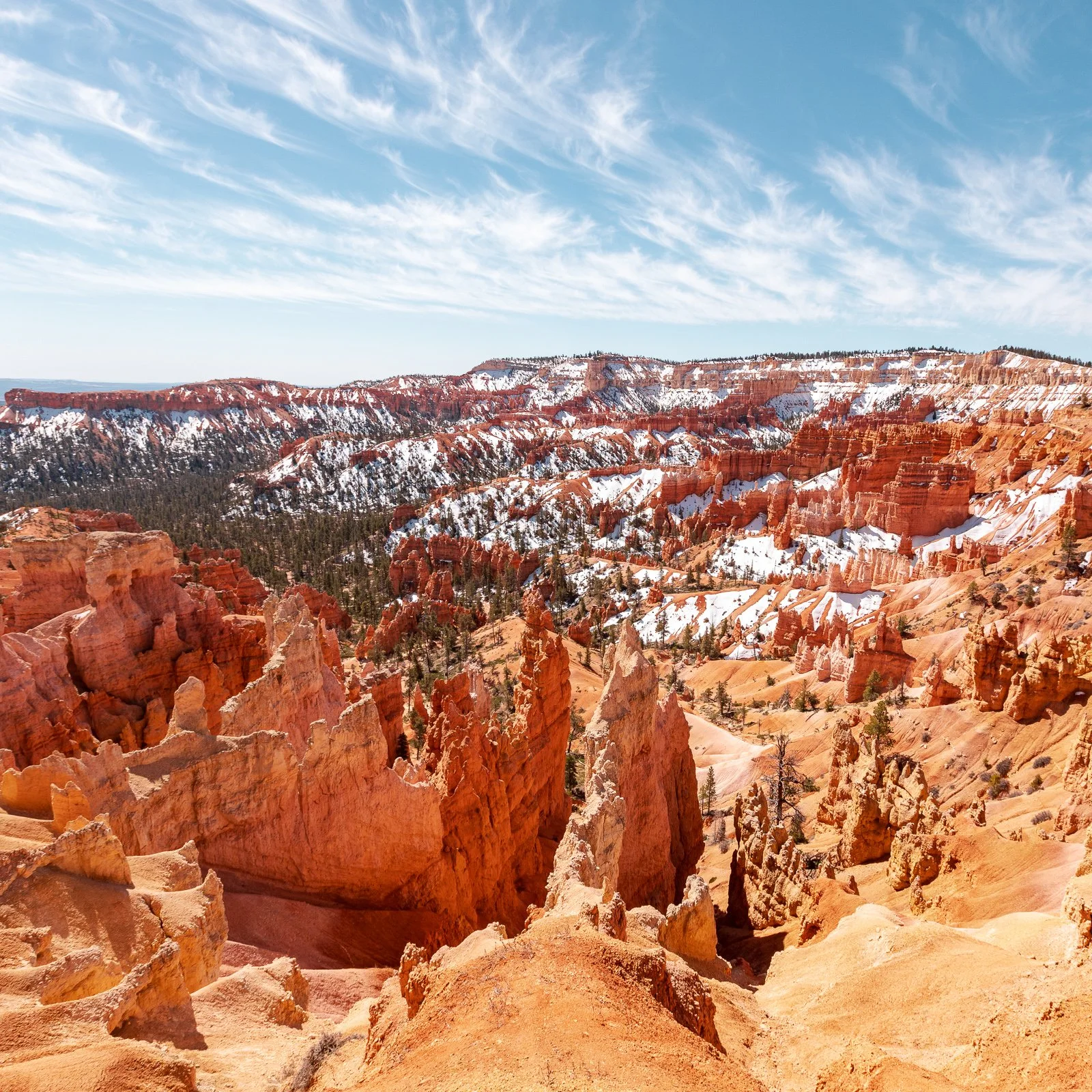 Canyon rocheux avec formation rocheuse rouge, des arbres verts par endroit, sous un ciel bleu avec des nuages blancs.