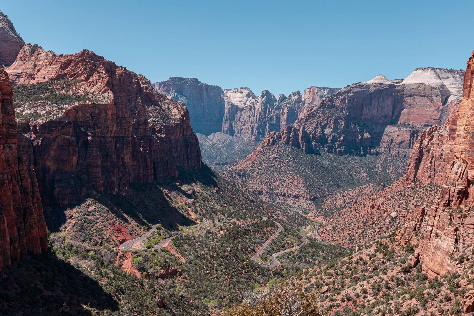 Vallée de montagnes avec des formations rocheuses rouges et blanches, et une route sinueuse en bas.